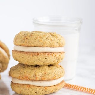 A stack of peanut butter whoopie pies with cream cheese frosting and a glass of milk.