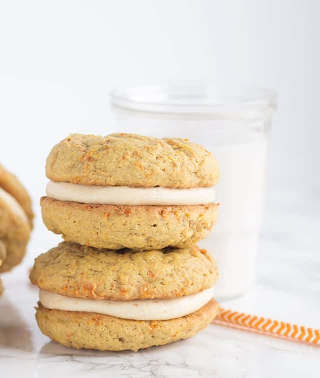 A stack of peanut butter whoopie pies with cream cheese frosting and a glass of milk.