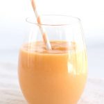 A tropical fruit smoothie served in a glass with a straw.