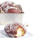 Vanilla cream-filled donuts covered in powdered sugar on a plate.