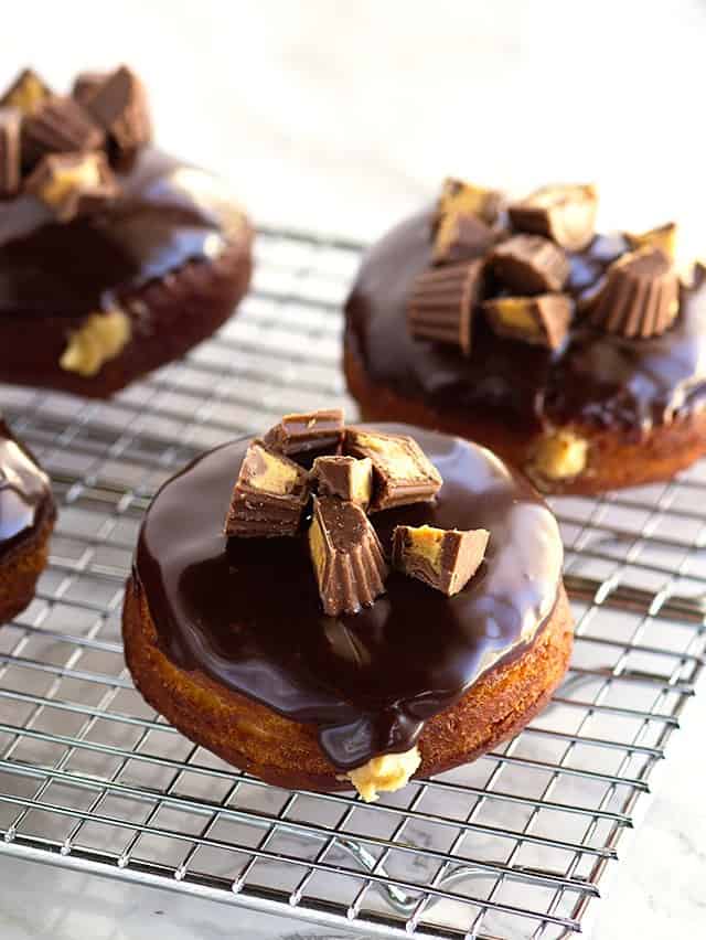 Chocolate glazed donuts with peanut butter filling arranged on a cooling rack.