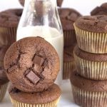 A stack of double chocolate muffins next to a glass of milk.