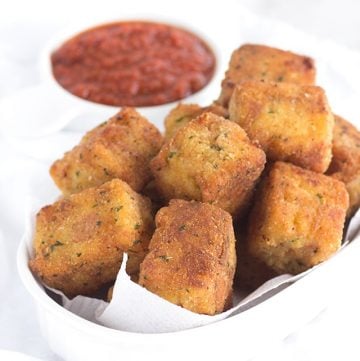 Cheesy tots, fried, in a white bowl with dipping sauce.