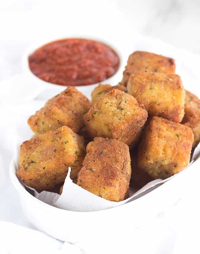 Cheesy tots, fried, in a white bowl with dipping sauce.