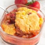 Strawberry cobbler in a warm glass dish with a spoon.