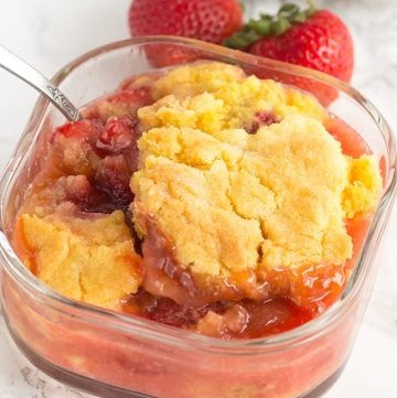 Strawberry cobbler in a warm glass dish with a spoon.