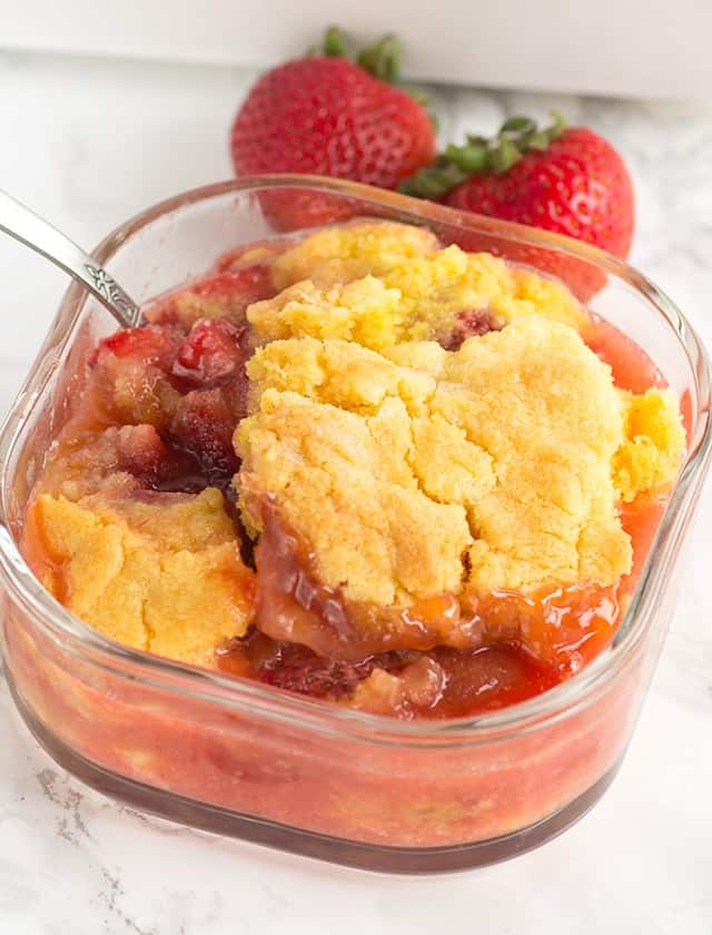 Strawberry cobbler in a warm glass dish with a spoon.