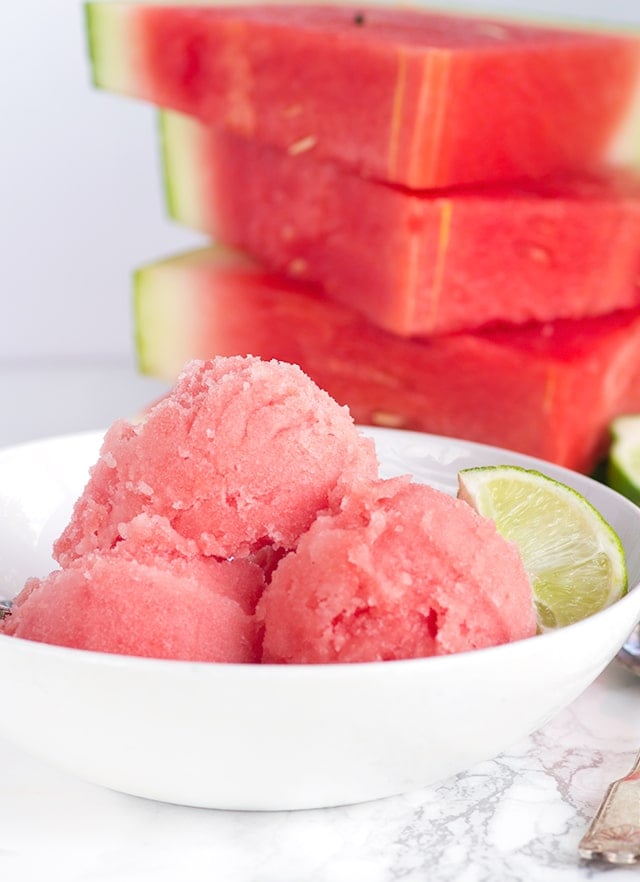 white bowl with fresh Watermelon Sorbet and a stack of fresh watermelon slices behind it