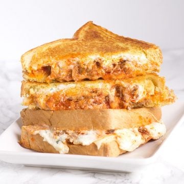 A stack of grilled cheese sandwiches, resembling a layered lasagna, on a white plate.