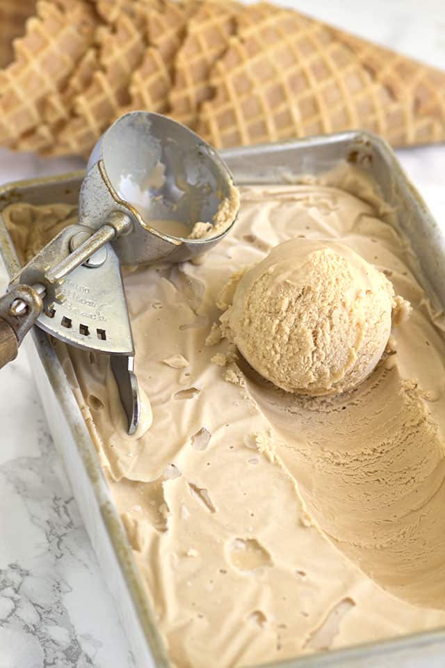 a scoop of homemade ice cream on top of the ice cream in a loaf pan with an ice cream scoop behind it