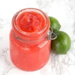 A jar of Raspberry Lime Curd with limes next to it.