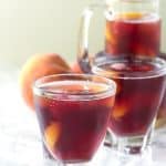 Three glasses of peach sangria with a raspberry twist, served on a sleek marble table.