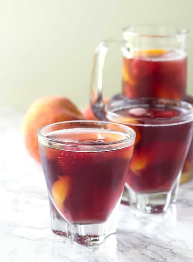 Three glasses of peach sangria with a raspberry twist, served on a sleek marble table.