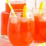 Two glasses of strawberry lemonade with straws and lemons.