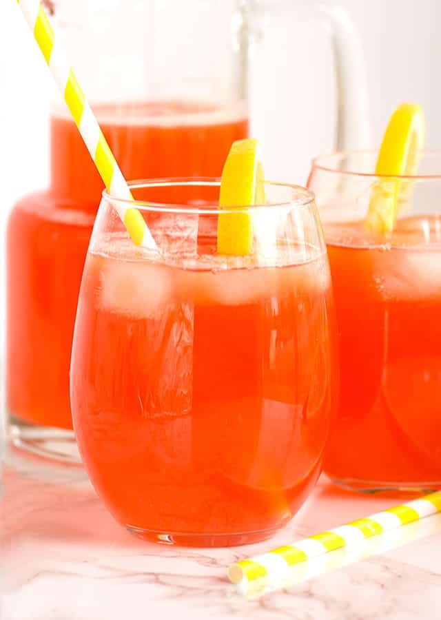 Two glasses of strawberry lemonade with straws and lemons.