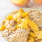 Skillet Peach Cobbler served on a white plate with fresh peaches.