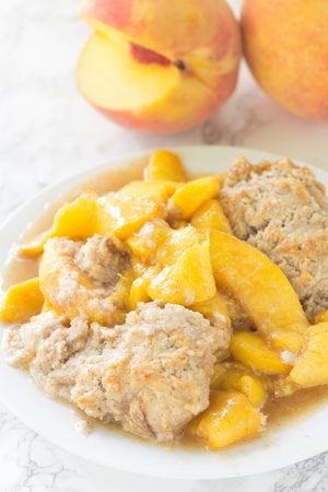 Skillet Peach Cobbler served on a white plate with fresh peaches.