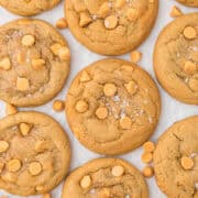 Golden brown butterscotch cookies topped with chips and flakes of sea salt, arranged on a white surface.