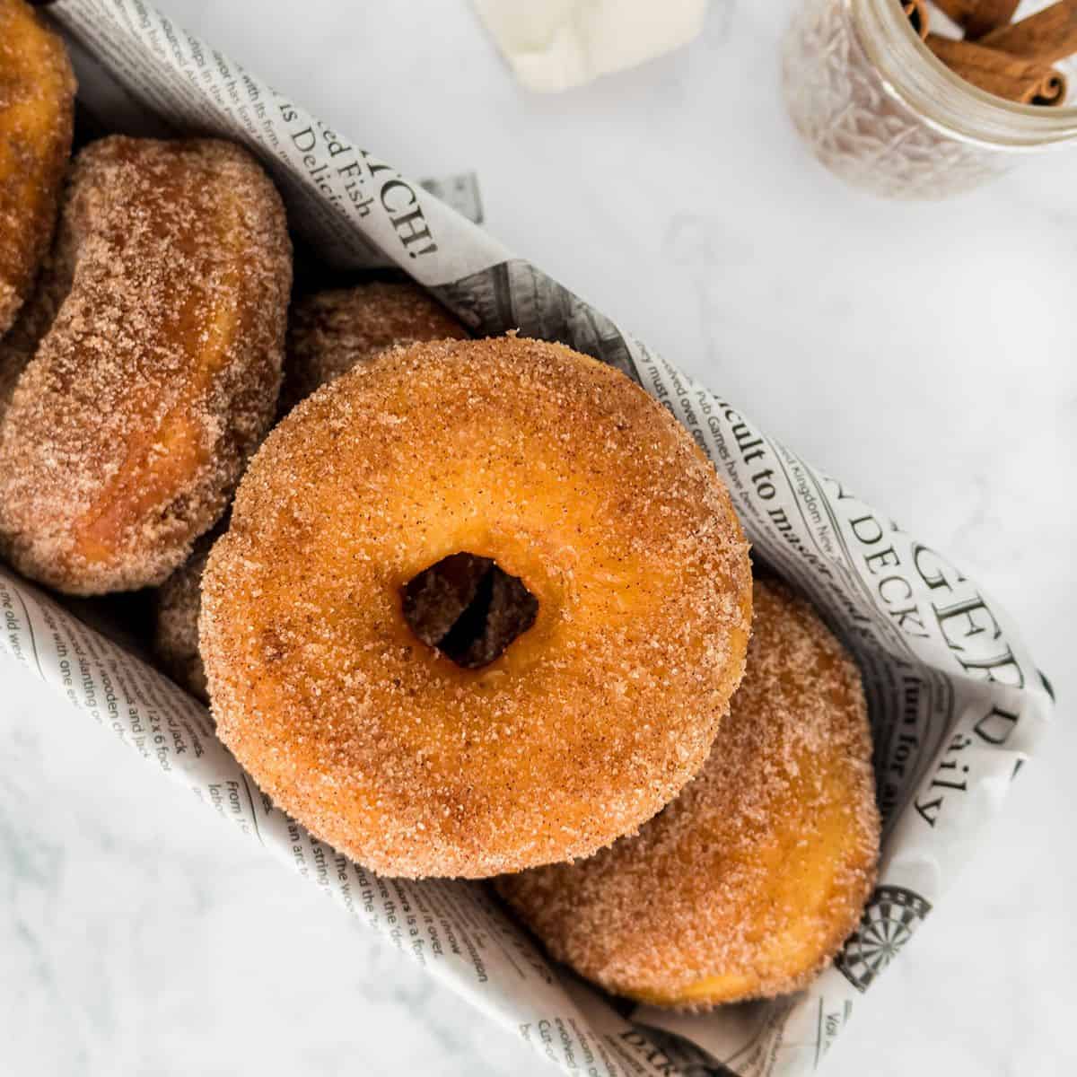 A tray lined with newspaper holds several cinnamon sugar Potato Donuts, with one donut prominently displayed on top.