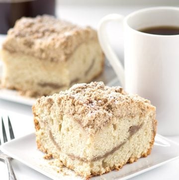 A slice of old fashioned coffee cake on a plate next to a cup of coffee.