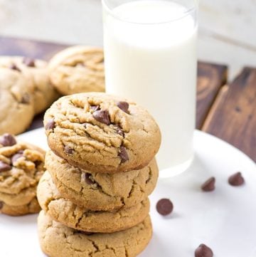 A stack of peanut butter chocolate chip cookies next to a glass of milk.