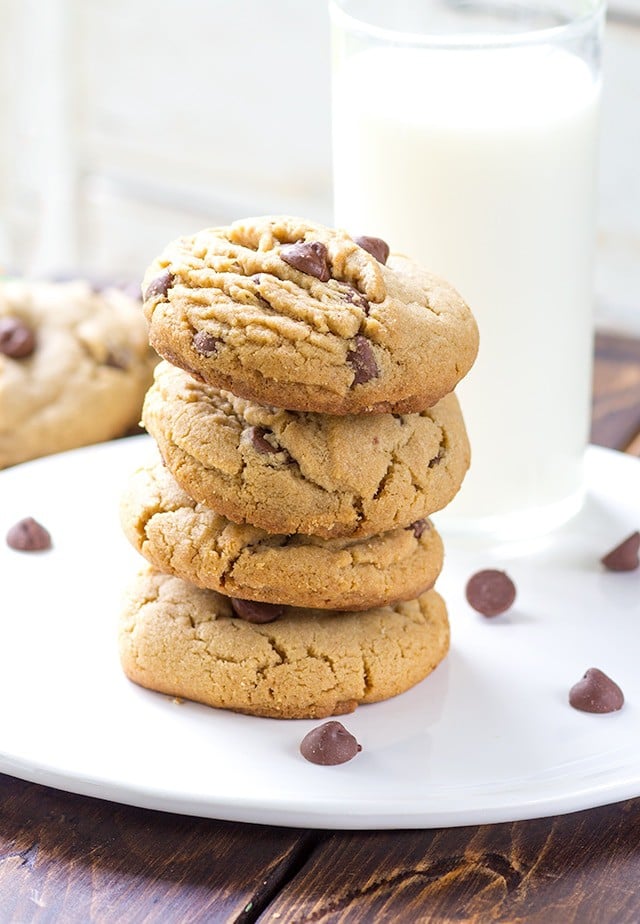 4 peanut butter chocolate chip cookies stacked onto a white plate. Chocolate chips scattered around the plate