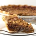 A slice of chocolate pecan pie, served with a fork on a plate.