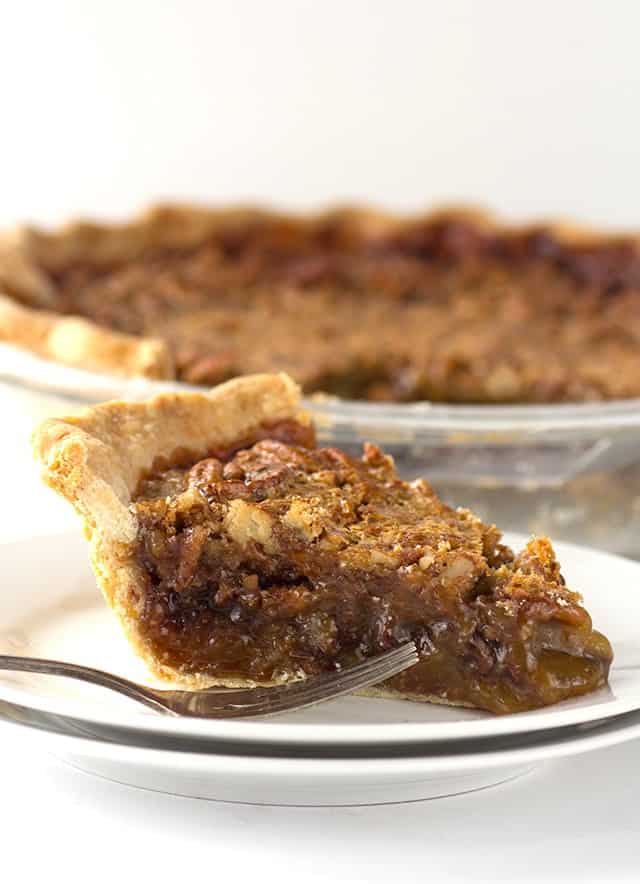 A slice of chocolate pecan pie, served with a fork on a plate.