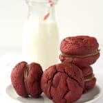Red velvet sandwich cookies on a plate with a glass of milk.