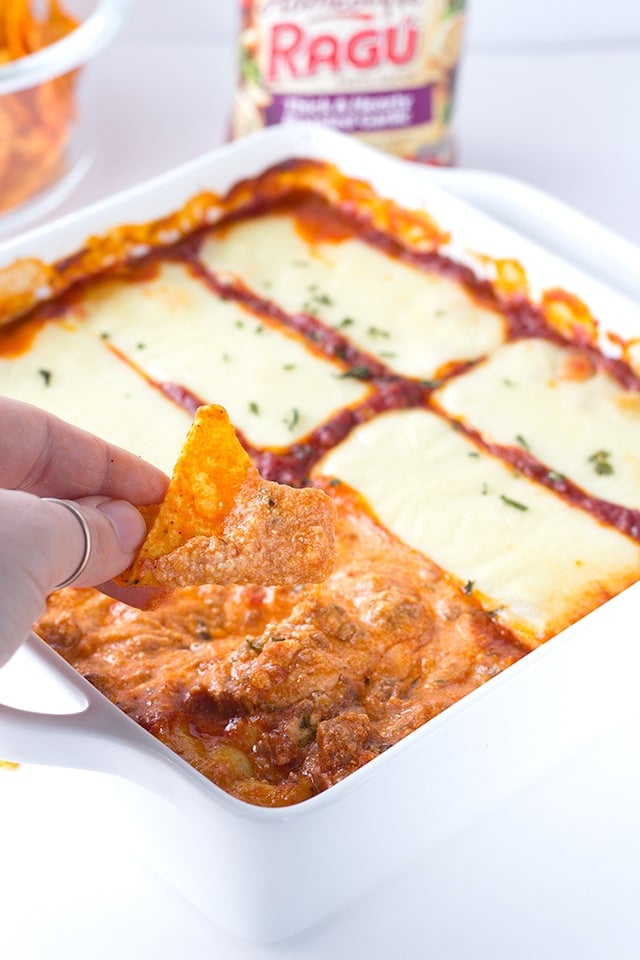 dipping tortilla chips into cheesy lasagna dip