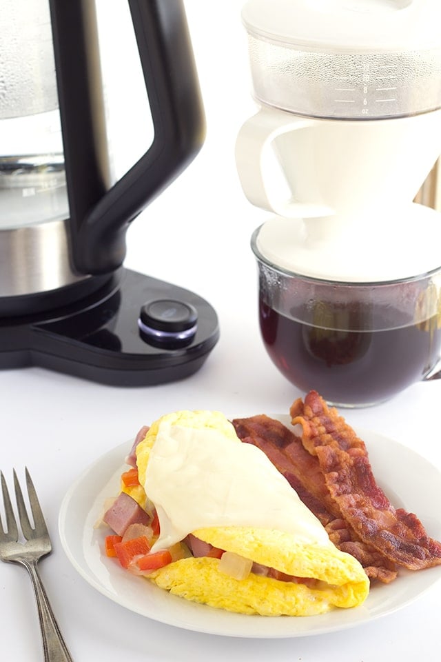 western omelet and bacon on a white plate with a fork and a coffee