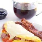 western omelet and bacon on a white plate with a cup of coffee behind it