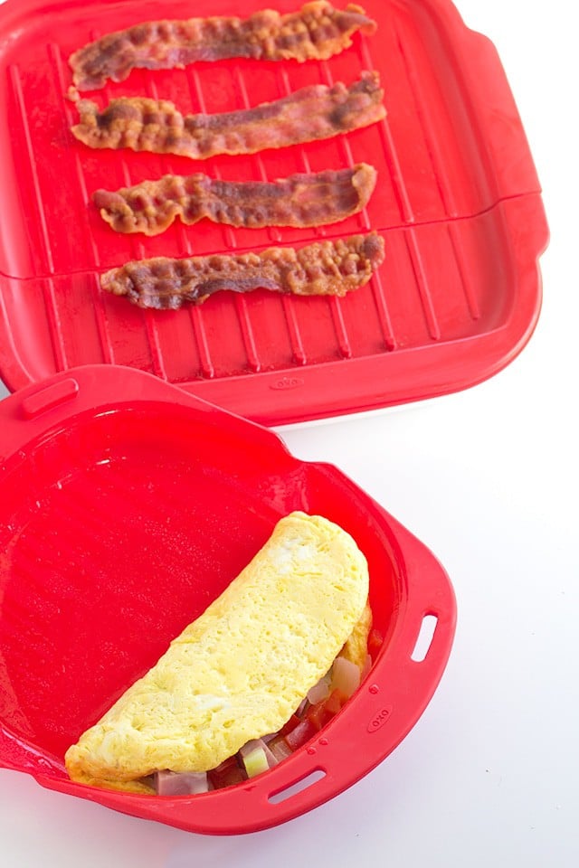 omelet in a red microwave dish with a bacon crisper next to it on a white surface