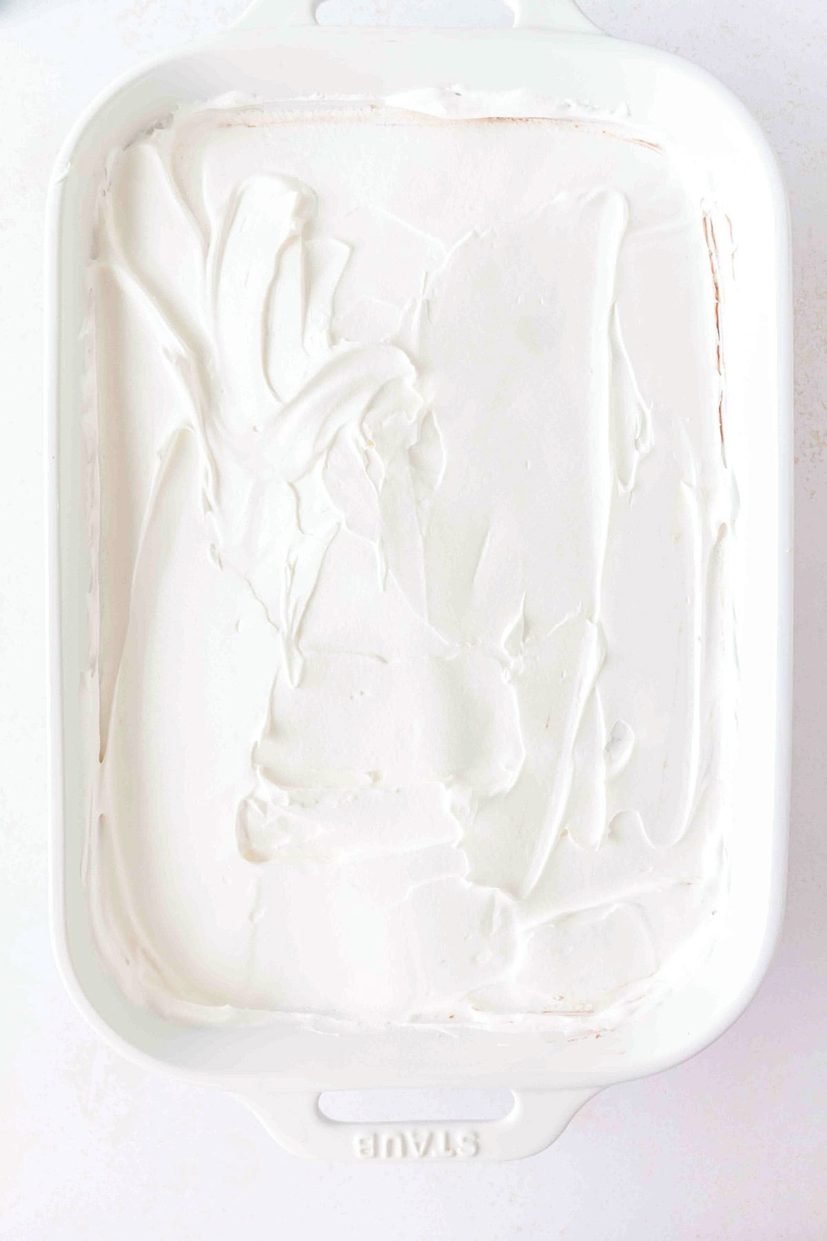 A white baking dish filled with Chocolate Peanut Butter Layer Dessert, topped with a thick, smooth layer of white whipped topping.