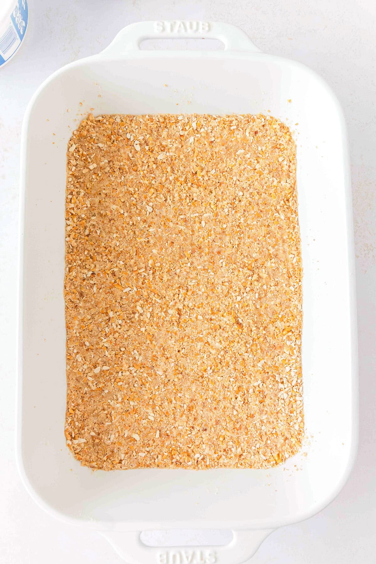A white baking dish filled with an even layer of crushed graham cracker crumbs, ready to become the base for a delicious Chocolate Peanut Butter Layer Dessert.