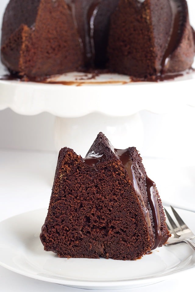 slice of Chocolate Whiskey Cake on a plate with the rest of the whiskey bundt cake on a cake plate behind it