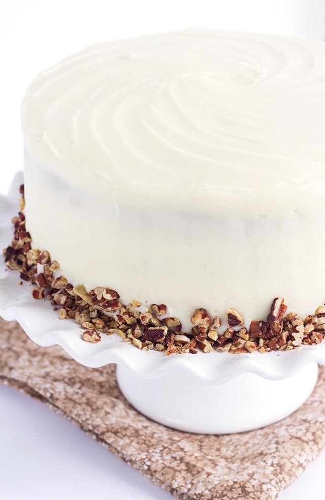 Pineapple Carrot Cake with Cream Cheese Frosting, garnished with toasted almonds, on a white cake stand.