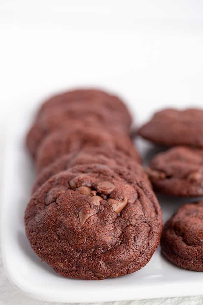A row of Double Chocolate Chip Pudding Cookies is arranged neatly on a white rectangular plate.