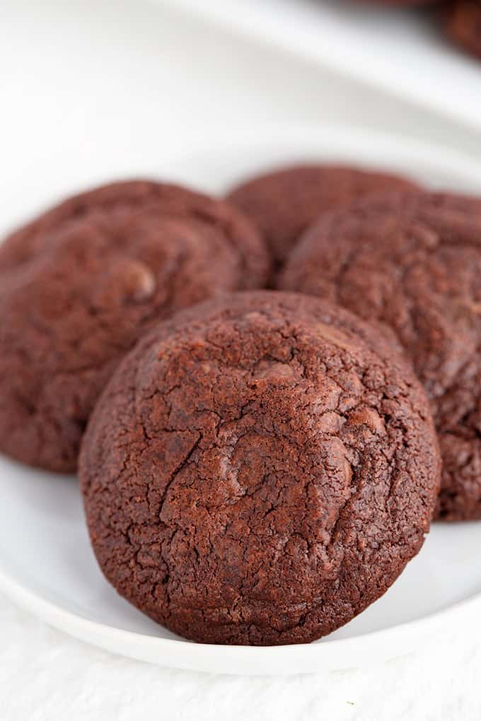A close-up of several Double Chocolate Chip Pudding Cookies stacked on a white plate.