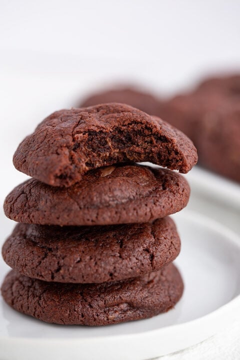 A stack of three Double Chocolate Chip Pudding Cookies on a white plate, with the top cookie showing a bite taken out.