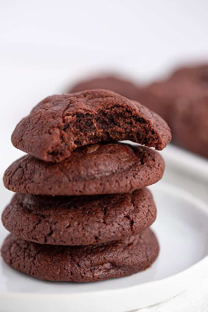 A stack of three Double Chocolate Chip Pudding Cookies on a white plate, with the top cookie showing a bite taken out.