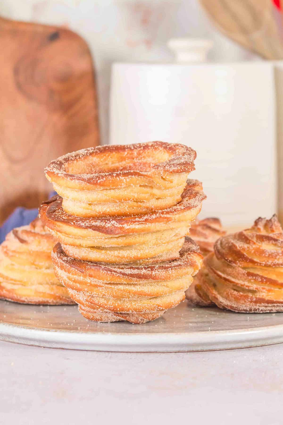 A stack of four golden, sugar-coated cronut pastries sits on a plate, with two more cronuts beside them—reminiscent of irresistible Churro Ice Cream Cups.