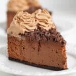 A slice of rich Triple Chocolate Cheesecake topped with chocolate shavings and swirls of chocolate mousse on a white plate.