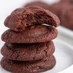 A stack of three Double Chocolate Chip Pudding Cookies sits on a white plate, with a fourth cookie on top showing a bite taken out of it.