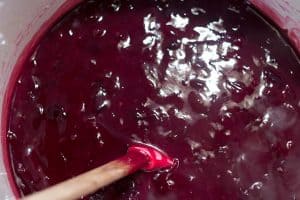 A bowl of blueberry sauce being stirred with a wooden spoon.