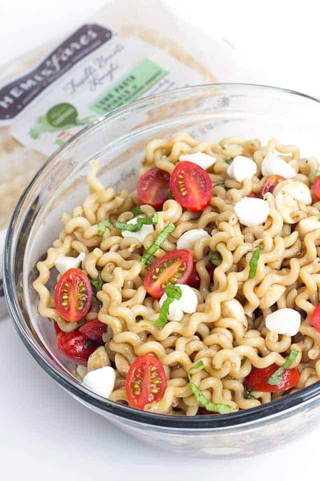 big salad bowl full of caprese pasta salad garnished with fresh cherry tomato halves