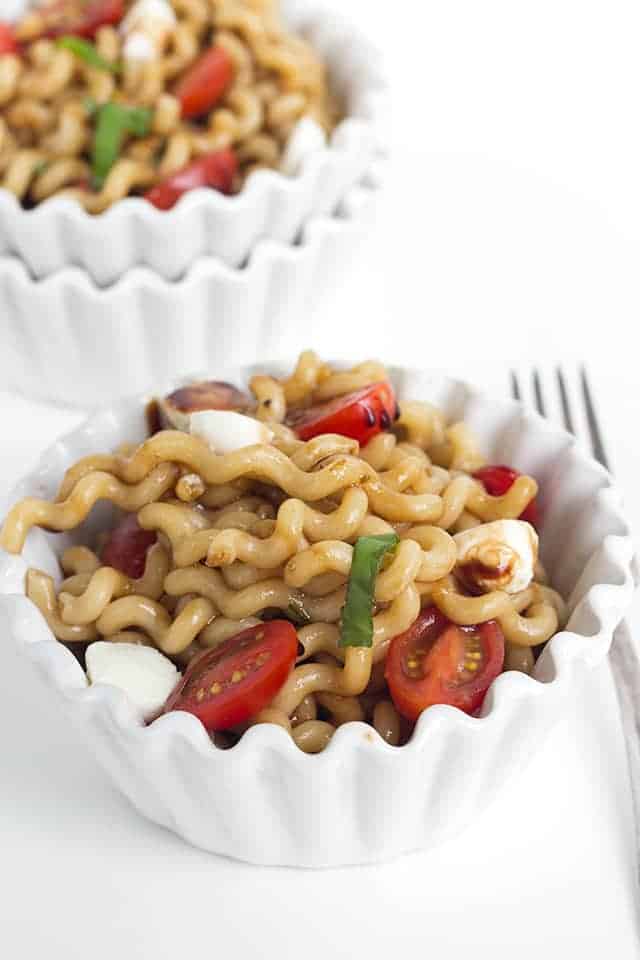 Caprese Pasta Salad - Pasta salad fanatics, you have to try out this one! There's a balsamic vinaigrette dressing, long pasta spirals, fresh mozzarella pearls, halved cherry tomatoes, and ribbons of basil! It's the perfect summer salad for picnics! #summersalad #caprese #foodrecipes #saladrecipes #pastasalad #sidesalad #sidedish white ceramic bowls with scalloped rims are filled with caprese pasta salad