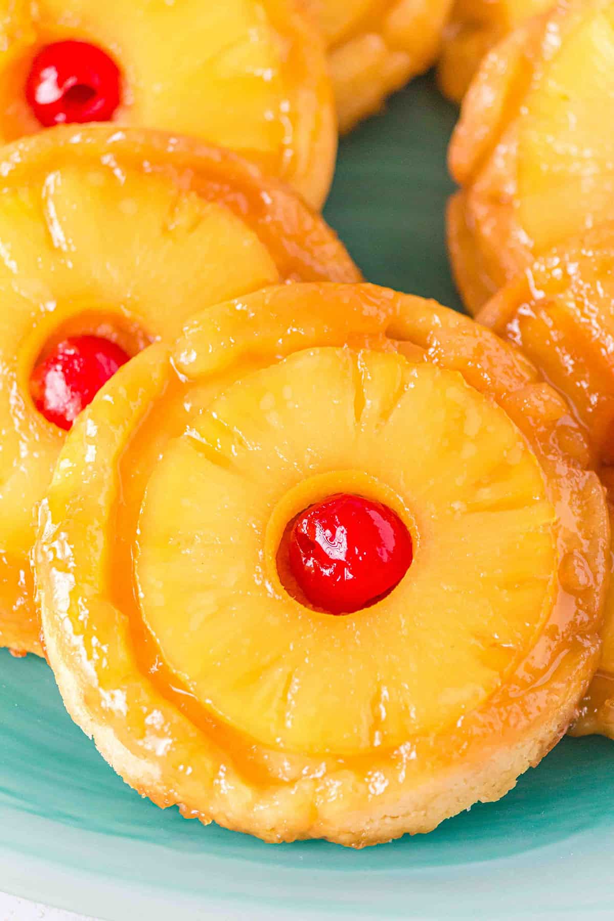 Mini pineapple upside-down cakes topped with pineapple rings and cherries, reminiscent of Pineapple Upside Down Sugar Cookies, arranged on a blue plate.