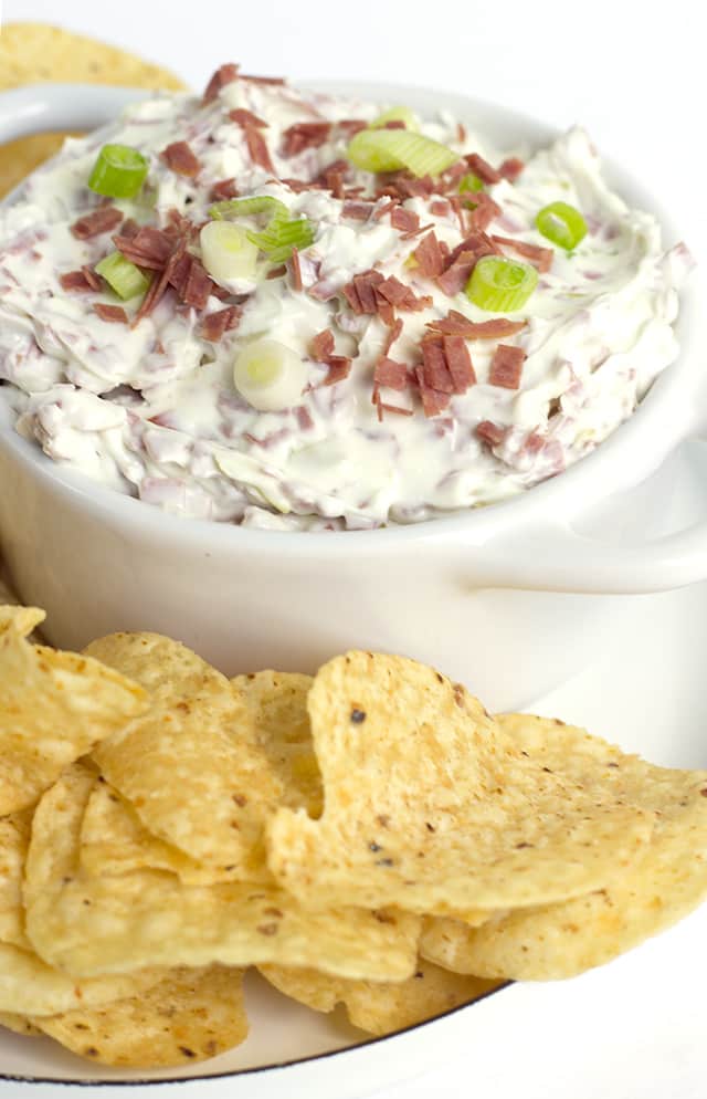 Chipped Beef Dip - This chipped beef dip recipe makes an amazing appetizer for any party. It has dried beef, green onions, and peperoncini in it. It goes great with veggies and bread! This is an easy chip beef recipe that uses dried beef. #appetizer #diprecipe #gamedayrecipes #gamedayfood #partyfood white bowl of Chipped Beef Dip and corn tortilla chips for dipping