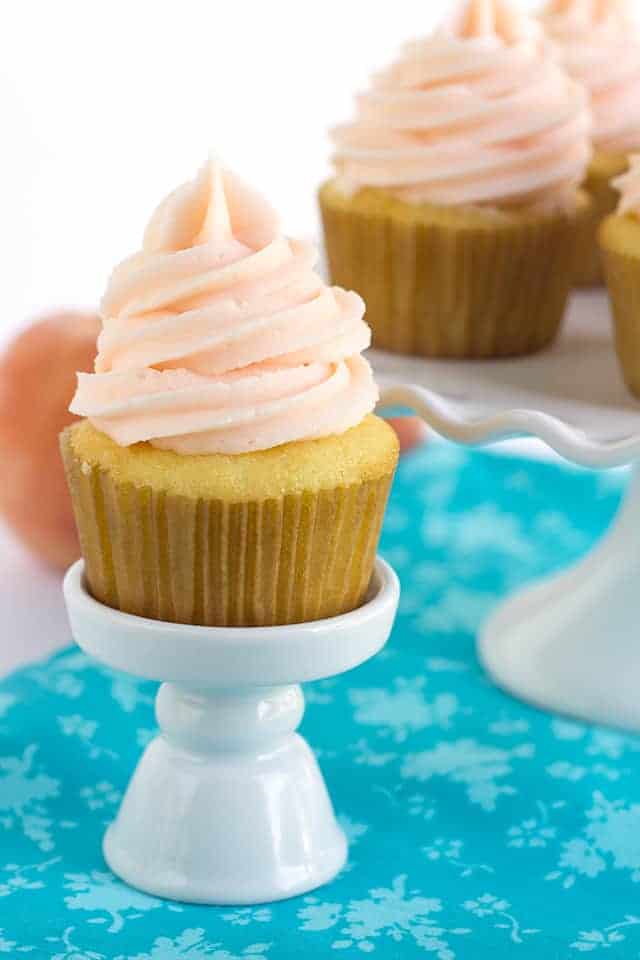 Yellow Cupcakes with Peach Cream Cheese Frosting - These yellow cupcakes with peach cream cheese frosting need to happen at every party. The yellow cake is so light and fluffy and the peach cream cheese frosting has a nice pop of flavor! Did I mention that peach colored frosting? #cookiedoughandovenmitt #cupcakes #cupcakerecipe #yellowcake #vanillacake #vanillacakerecipe #dessertfoodrecipes Yellow cupcakes on a small cupcake stand